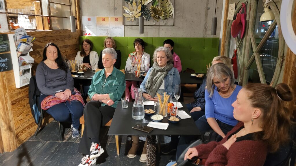Lebe(n) unverfälscht im Bioladen: Einige Anwesende bei einer Visualisierungsübung. 5 Frauen sitzen mit geschlossenen Augen an den Tischen im Bioladen Marias Biotreff.
